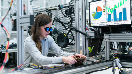 An engineer examining a bowl of roasted coffee in an industrial setting with a monitor displaying graphs and charts.