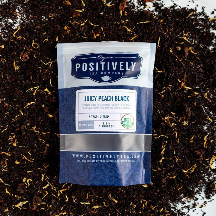 Juicy Peach Black Organic Tea, 4 oz resealable bag surrounded by loose leaf tea and peach accents, highlighting sweet, fruity notes.